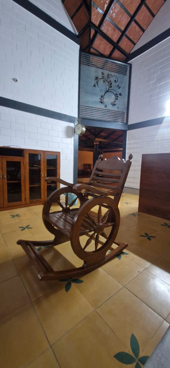 A dark wooden rocking chair with large wheels rests on a floor adorned at Aqua Terra Villas - Belur, Sakleshpur